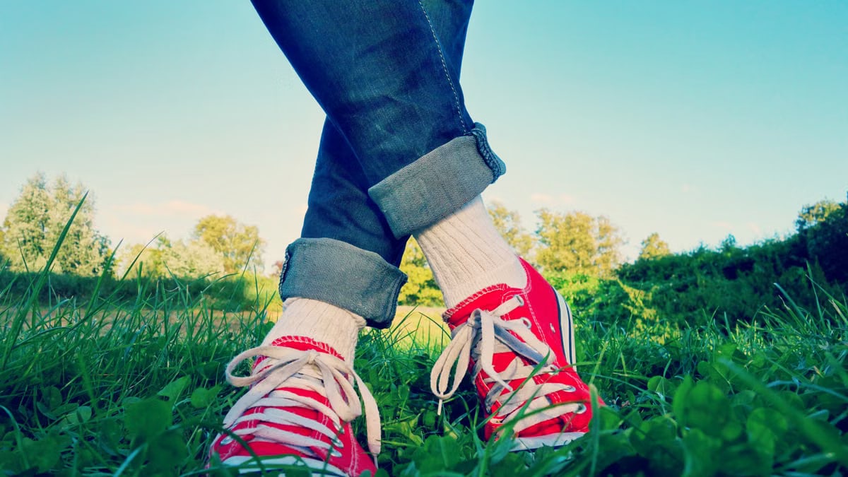 Stylish jeans and red sneakers captured in an outdoor grassy setting, showcasing casual fashion.